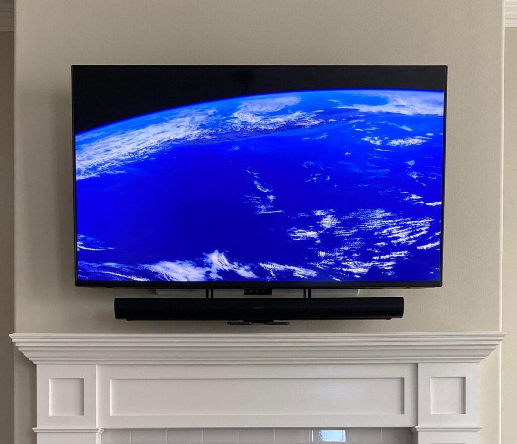 TV mounted above a white fireplace mantel with a soundbar below it, no visible cables