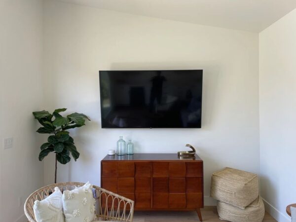 TV mounted on a bright white wall above a wooden dresser